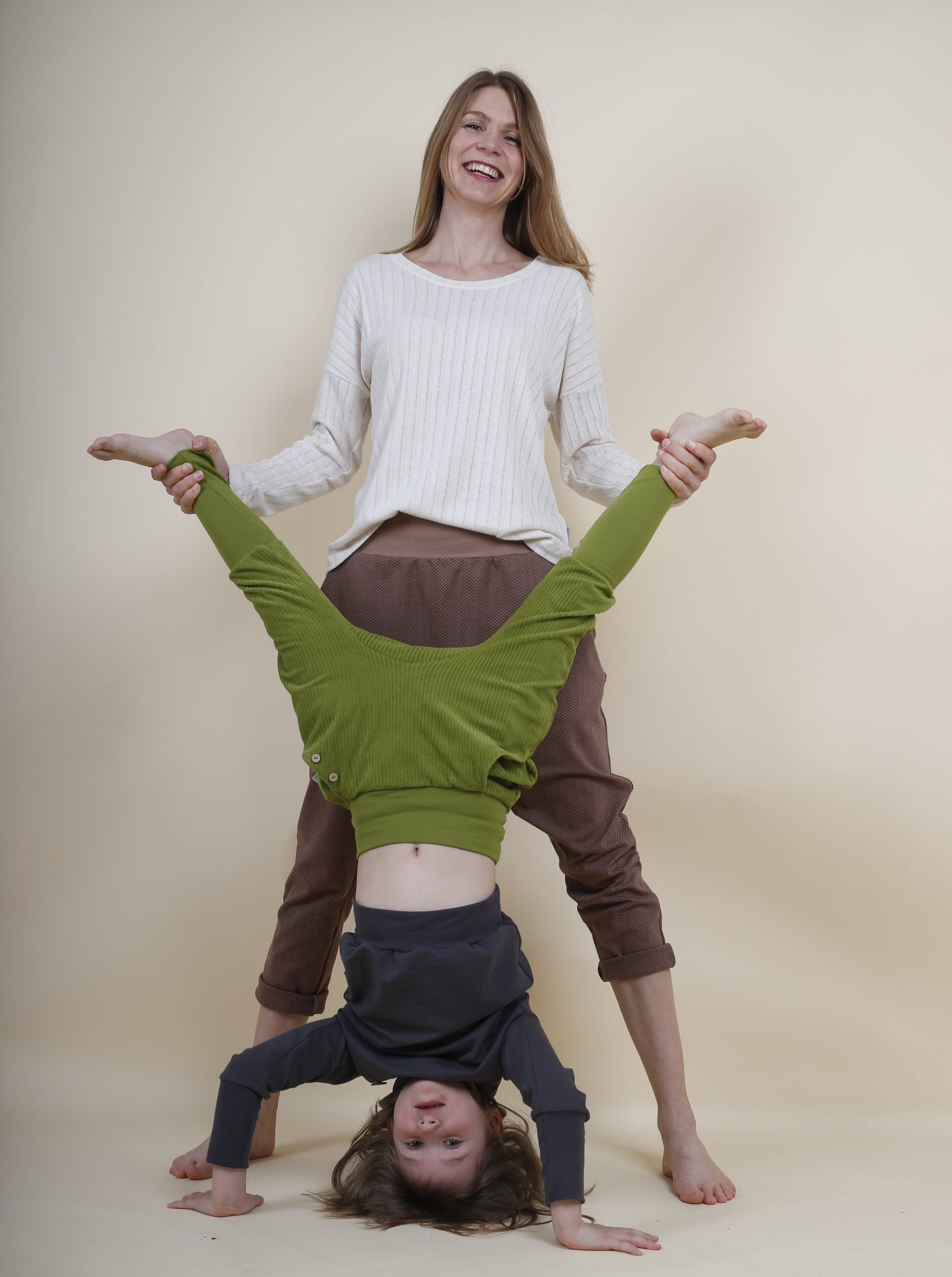 Mutter und Tochter albern herum das Kind macht einen Handstand, sie tragen nachhaltige Kleidung von tibelinchen