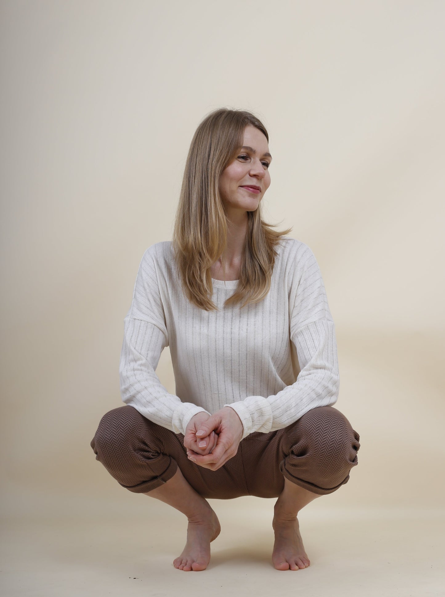 Frau hockt und zeigt ihr schönes Outfit, sie at ein Langarmshirt aus Leinenstrick und eie Pumphose für Damen an