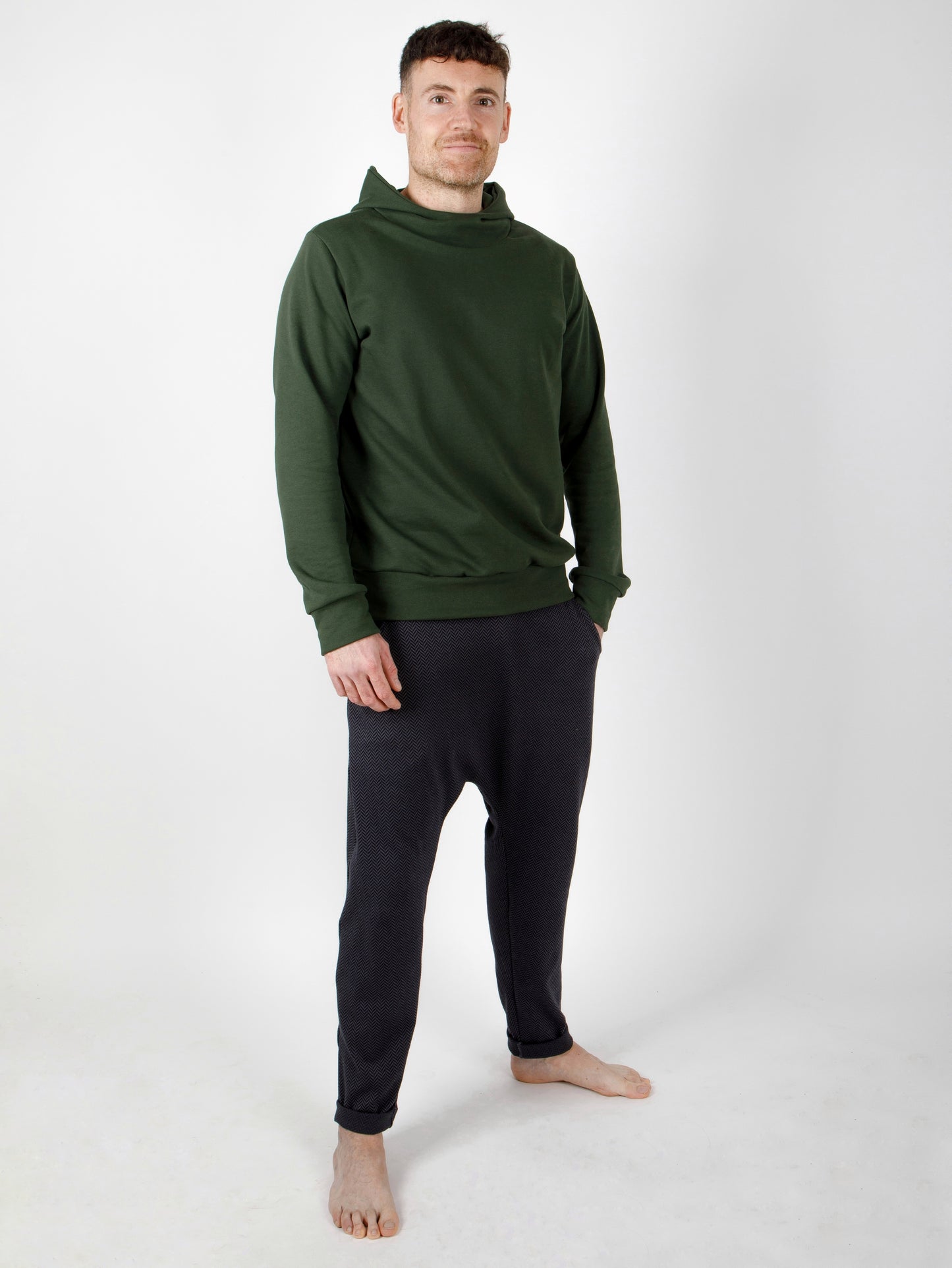 Ein Mann trägt eine Herrenhose und ein Oberteil für Herren mit Kapuze aus zertifizierter Biobaumwolle