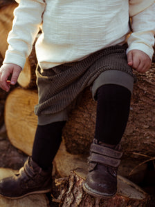Kind sitzt auf einem Holzstapel unf trägt eine Shorts aus Biobaumwolle