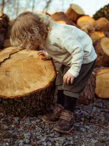 Kind schaut sich im Wald einen Baumstamm an und trägt eine Shorts 