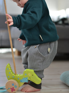 Baby spielt mit Holzspielzeug und trägt einen petrolfarbenen Strickpullover