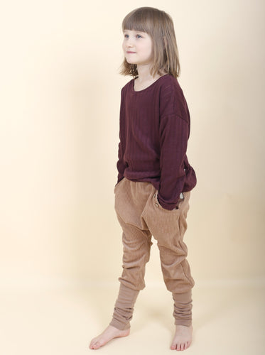 Kind trägt ein bordeaux farbenes Oberteil mit einer hellen Hose