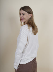 Dame trägt weisses Langarm-Shirt Leinenstrick zu brauner Haremshose, Ansicht von links hinten