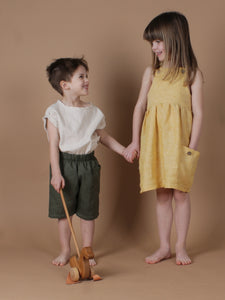 Zwei Kinder lächeln sich an und haben ein neutrales Outfit aus Leinen an