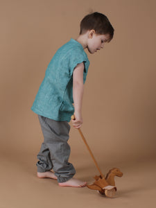 Kind trägt petrolfarbenes Leinenshirt und spielt mit einem Holzspielzeug