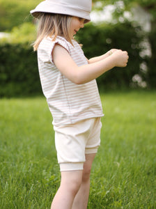 Ein Kind spielt mit einem Gänseblümchen und trägt eine nachhaltige Shorts aus Biobaumwolle