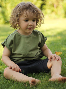 Junge sitz im Gras und hat neutrales sommeroutfit an