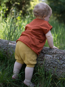 Ein Kleinkind spielt im Wald und trägt eine Shorts und ein Shirts aus Biobaumwolle