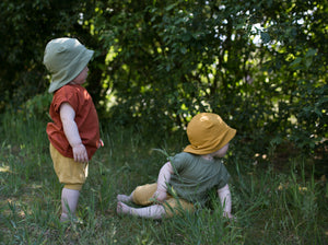 Zwei Kleinkinder sitzen im Gras und tragen neutrale Sommeroutfits