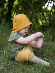 Ein Kleinkind sitzt im Gras, spielt mit seinem Fuß und trägt ein sommerliches Outfit von tibelinchen